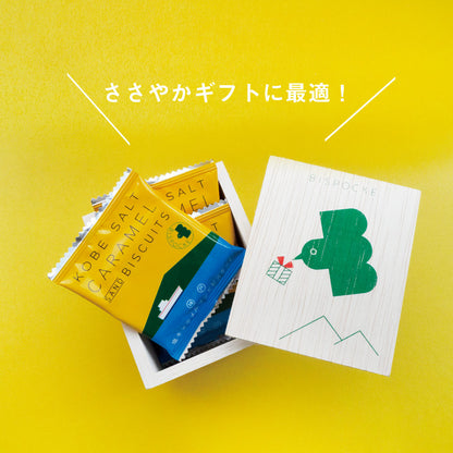 A wooden box with a green bird design on the lid. The bird has a small gift box in its mouth, and there is a yellow band with Japanese writing that says "arigato gozaimasu," which means "thank you very much." Inside the box, there are four individually wrapped salted caramel cookies.